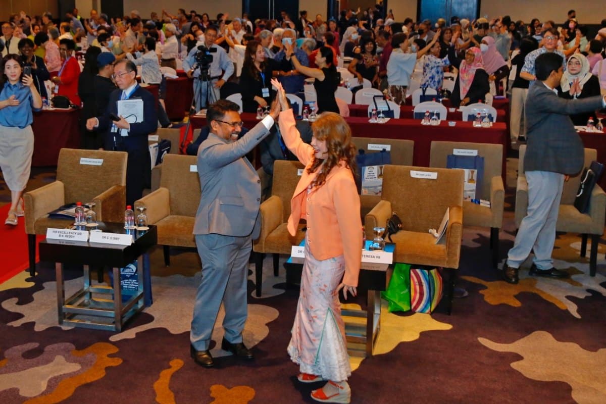 Teresa Hii in a peach jacket high-fives a colleague in a crowded conference hall while the audience stands and claps