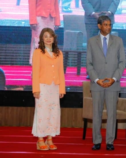 Teresa Hii standing on a conference stage in a peach jacket and floral skirt, facing the camera